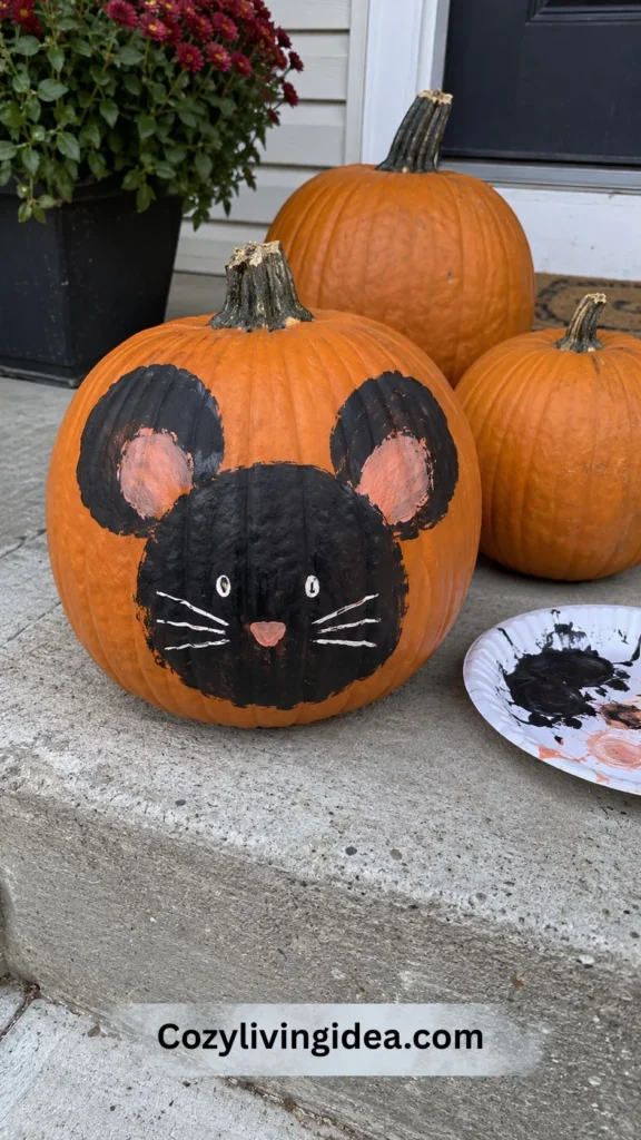 Cute mouse pumpkin painting idea with a hand-painted black face, rounded ears, whiskers, and pink details on an orange pumpkin